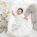 A cute one-month-old baby lying with plush toys on a bed, celebrating a special milestone.