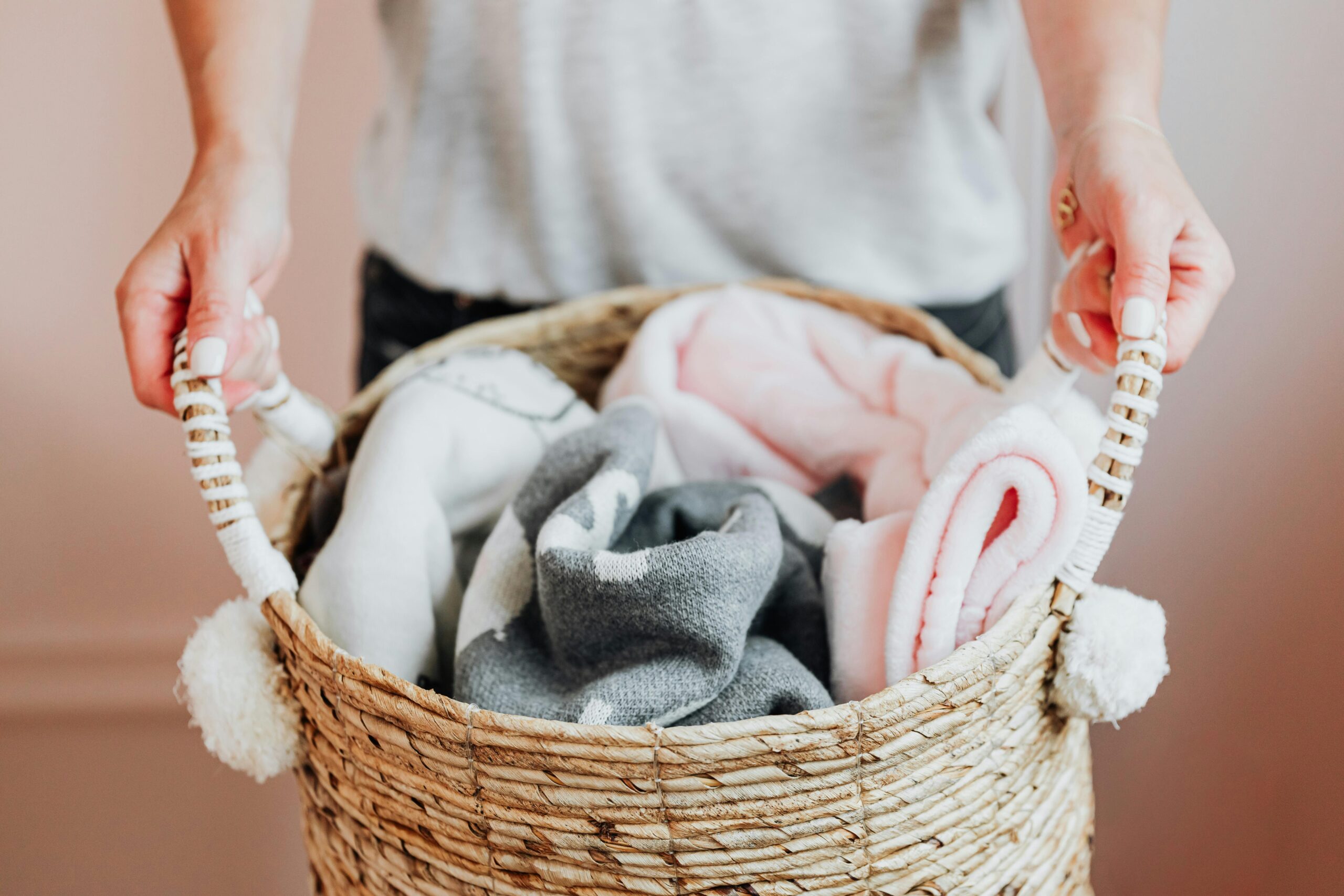 Close-up of hands holding a woven basket full of soft baby blankets indoors.